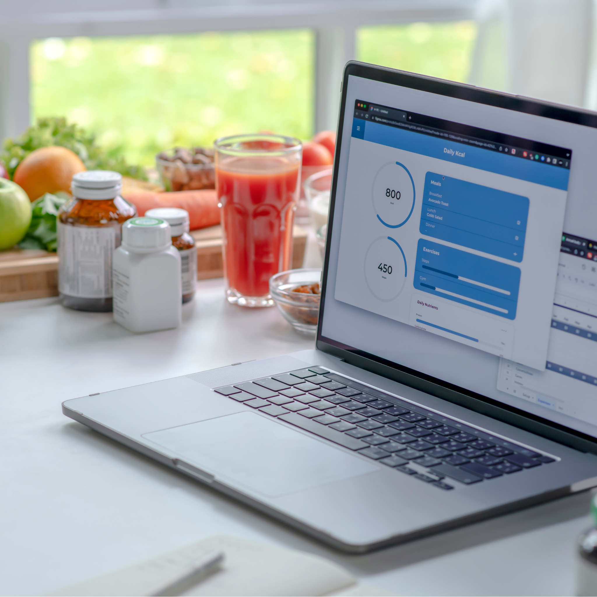 Laptop screen on a counter with supplement bottles and fresh fruit and veg in the background